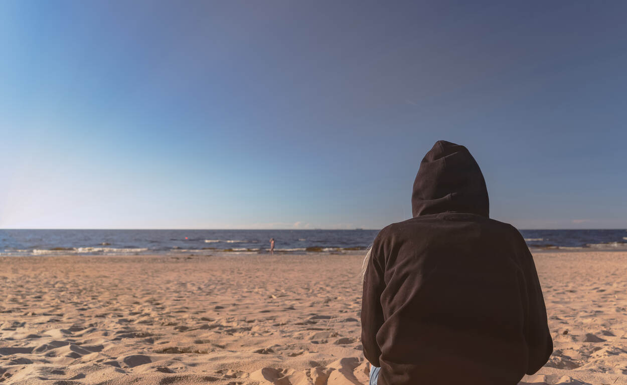 Een meisje zit op het strand met een zwarte hoody aan