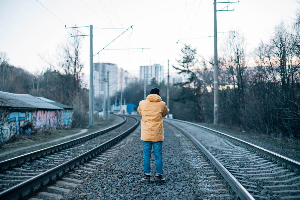 Een man met een gele jas loopt tussen de treinrails, van achteren gezien